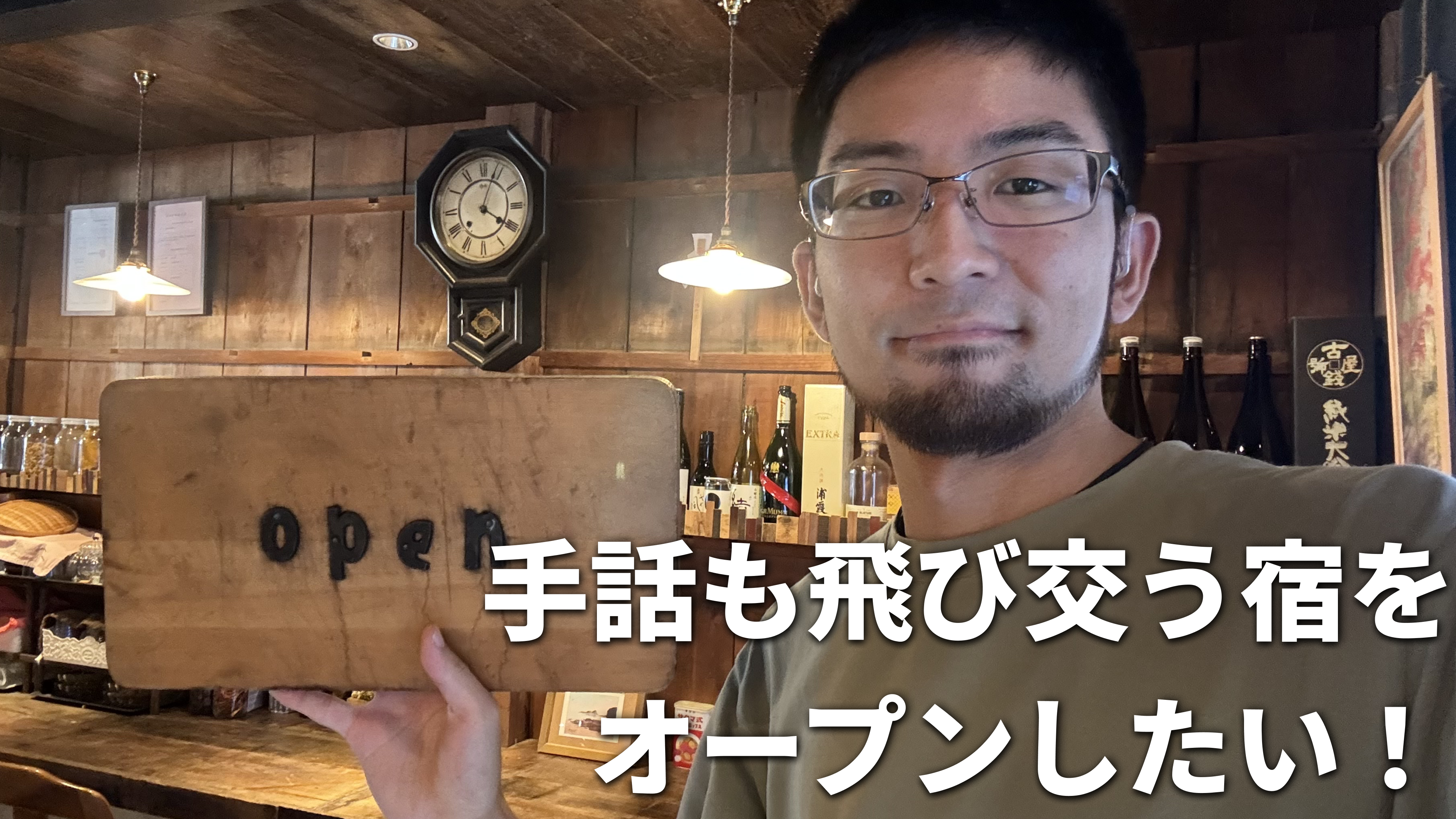 古民家ながらもオシャレな空間のヤマイロゲストハウスでにて竹花がopenと書かれた看板を手にしている様子を背景に、白文字で「手話も飛び交う宿をオープンしたい!」